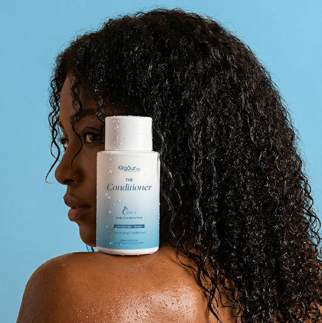 Woman with curly hair holding a bottle of 'The Conditioner' against a blue background