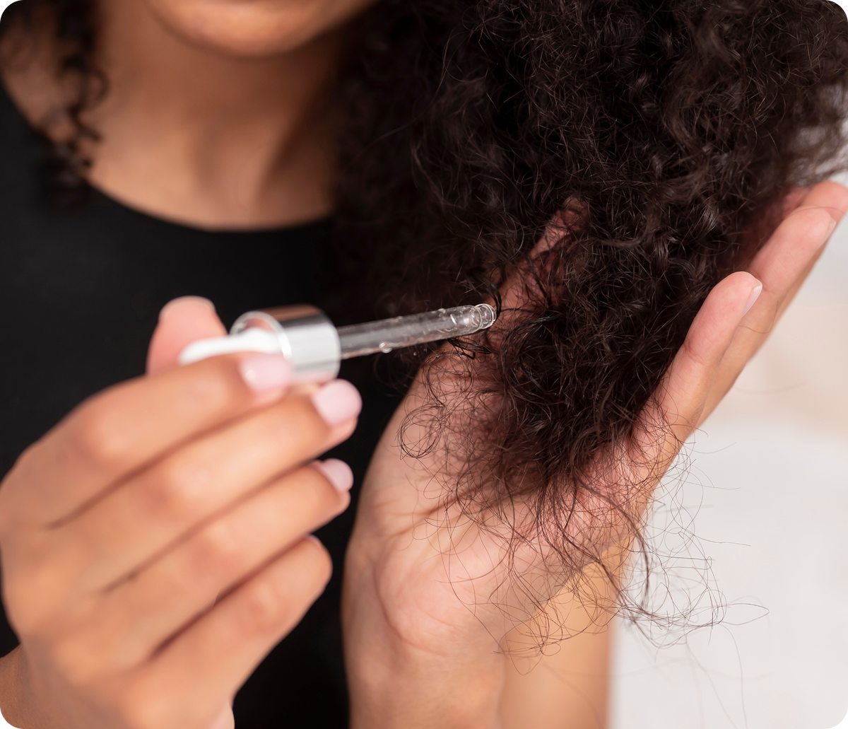 Close-up of a person applying hair serum with a glass dropper to dry curly hair
