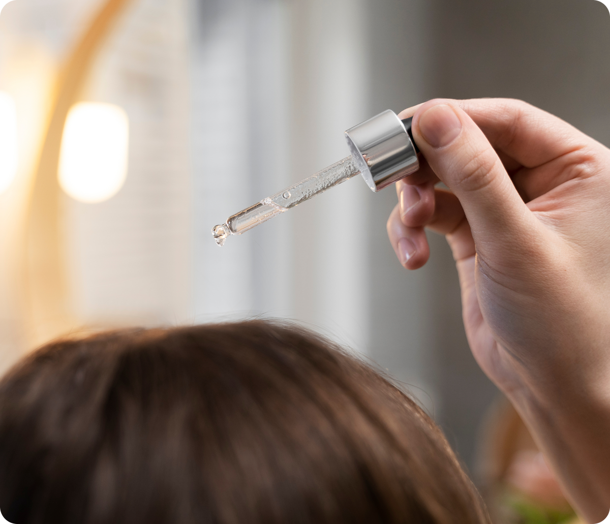 Close-up of a person applying hair serum with a glass dropper to dry curly hair
